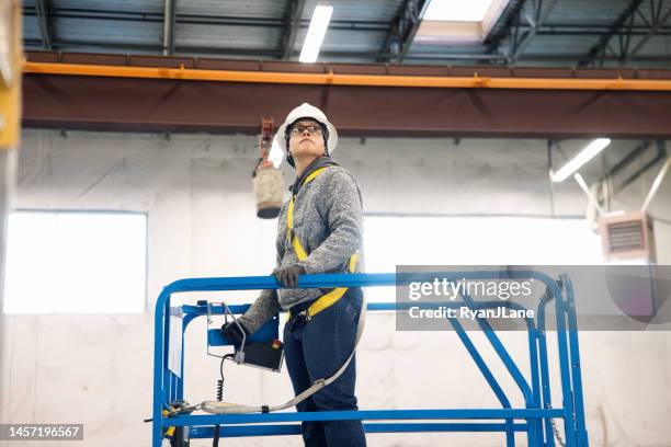 woman worker using aerial lift in warehouse setting - safety harness stockfoto's en -beelden