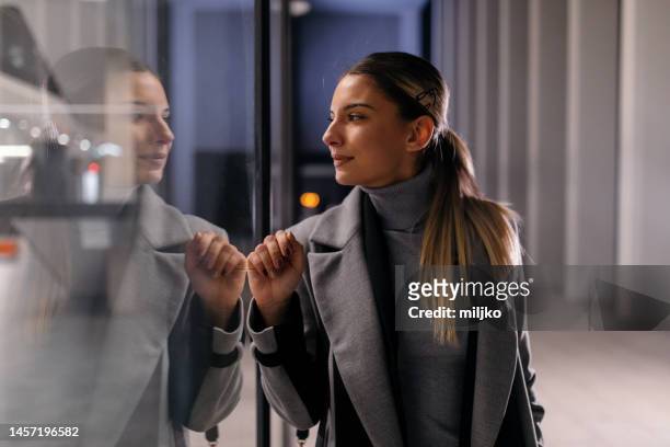 business woman walking outdoors and looking in window shop at night - window shopping stock pictures, royalty-free photos & images