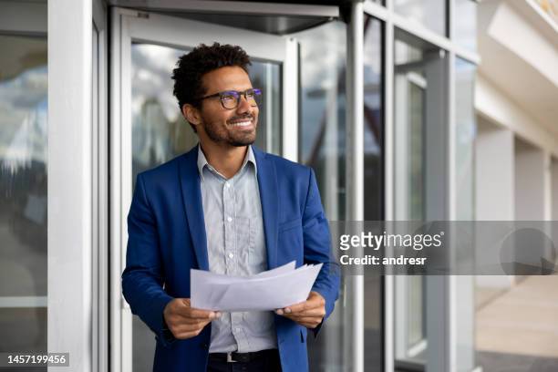 business man leaving an office building holding documents and smiling - entry draft portraits stock pictures, royalty-free photos & images
