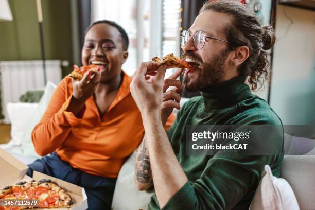 verschiedene freunde essen pizza im wohnzimmer - ungesunde ernährung stock-fotos und bilder