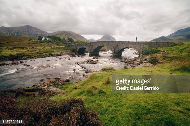 man on the sligachan old bridge in the scottish highlands landscape, isle of skye, scotland - mountain river stock pictures, royalty-free photos & images