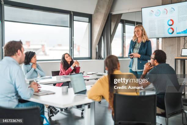 multi-ethnic entrepreneurs listen to female leader's presentation - 50s woman writing at table imagens e fotografias de stock