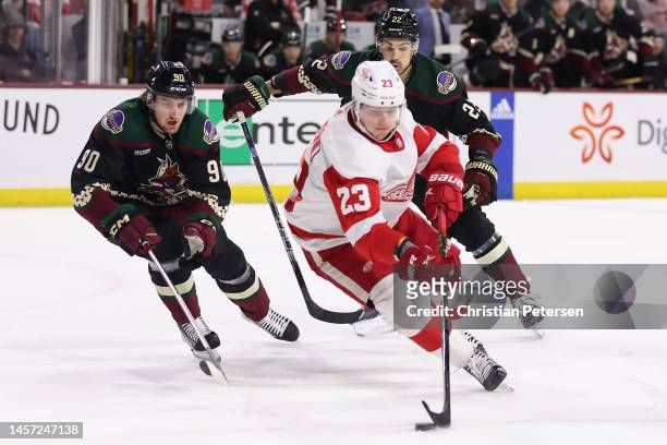 Lucas Raymond of the Detroit Red Wings skates with the puck under pressure from J.J. Moser and Jack McBain of the Arizona Coyotes during the first...