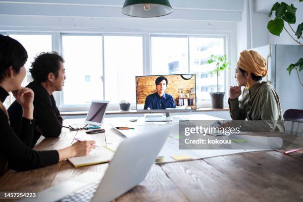 lässig gekleidete büroangestellte sitzen an einem tisch und haben eine videokonferenz - die neue normalität stock-fotos und bilder