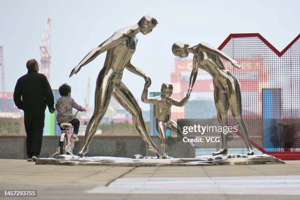 An elderly man guides a child on a bicycle nex to statues depicting a family on October 27, 2022 in Yantai, Shandong Province of China.