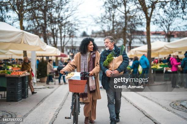latin curly hair woman and senior man strolling by the farmer's market on the weekend - agricultural fair stock pictures, royalty-free photos & images
