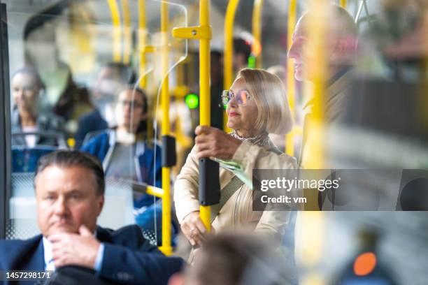 senior couple standing in bus and holding handrail, medium shot - rush hour stock pictures, royalty-free photos & images