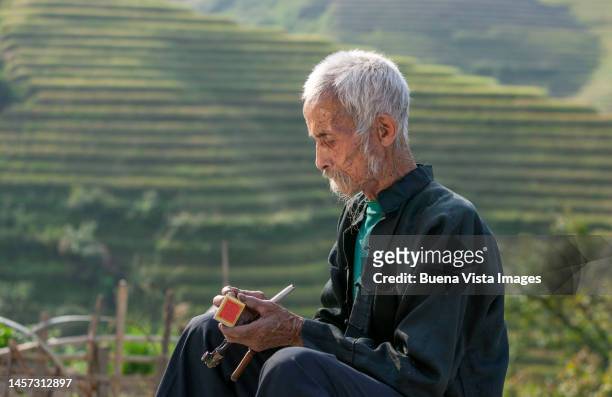 old chinese man lighting his pipe - bauer pfeife stock-fotos und bilder