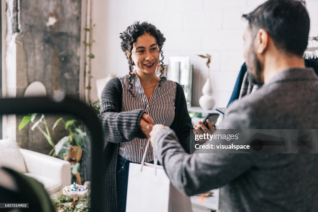 Indian man making a mobile payment in small business boutique