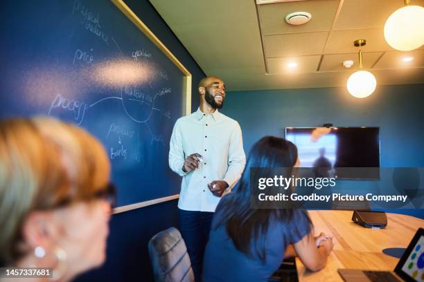businessman laughing while giving coworkers a marketing presentation in a board room - board room meeting stockfoto's en -beelden