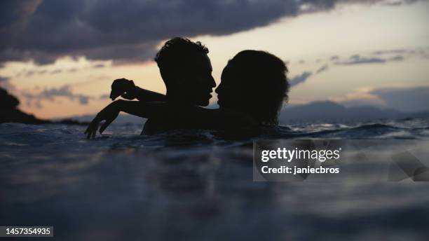 african ethnicity romantic heterosexual couple swimming and embracing in the sea at dusk - african american woman bath stock pictures, royalty-free photos & images