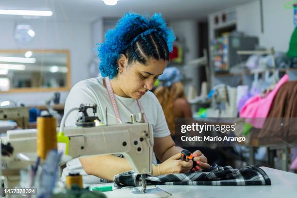 latin woman with blue hair seamstress by profession is sitting at her work station - designer clothing stock pictures, royalty-free photos & images