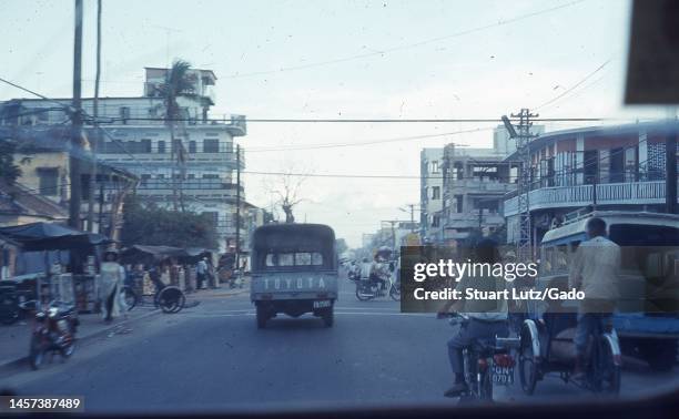 Wide-shot of cyclists, a tricycle, a Toyota truck, and pedestrians traveling on a busy urban street, Vietnam, 1971.