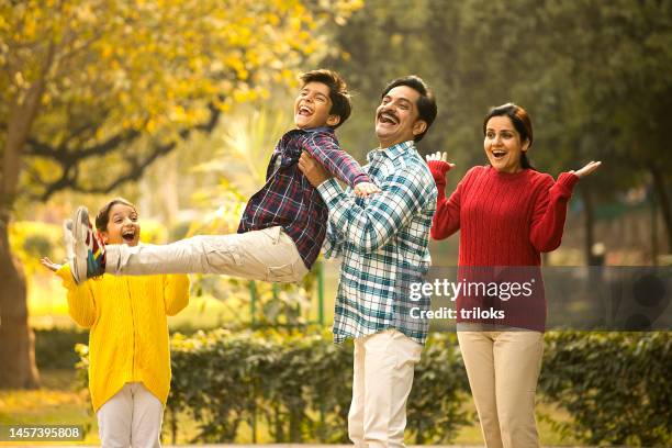 cheerful parents playing with children at park - india couple lift stock pictures, royalty-free photos & images