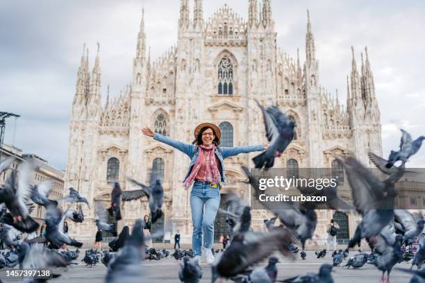 mulher nova na frente da catedral em milão com pombos voando ao redor - milan cathedral - fotografias e filmes do acervo