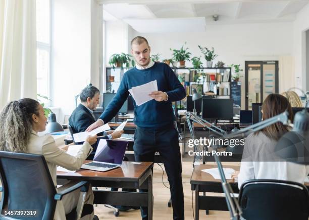 man giving handouts to diverse employees in open plan office - delegating 個照片及圖片檔