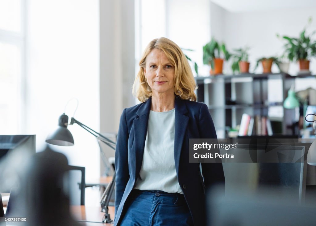 Portrait of a confident mature businesswoman standing by a desk in office