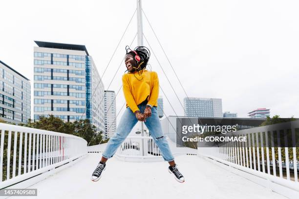 happy young woman jumping in the middle of a bridge and listening to music with headphones and looking to the side. woman with vitiligo. - woman full body isolated stock pictures, royalty-free photos & images