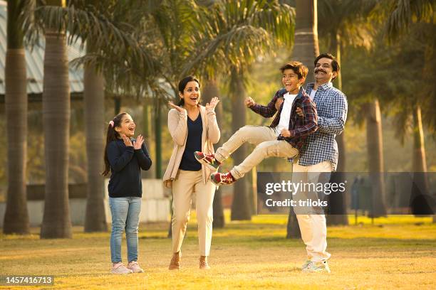 cheerful parents playing with children at park - india couple lift stock pictures, royalty-free photos & images