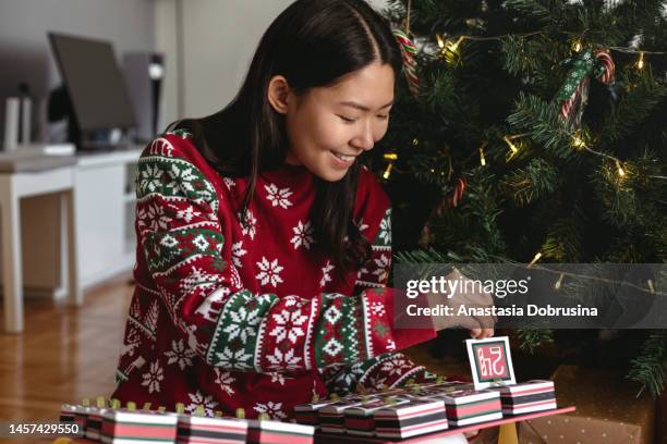 junge erwachsene asiatische frau öffnet geschenkboxen des weihnachtsadventskalenders - adventskalender stock-fotos und bilder