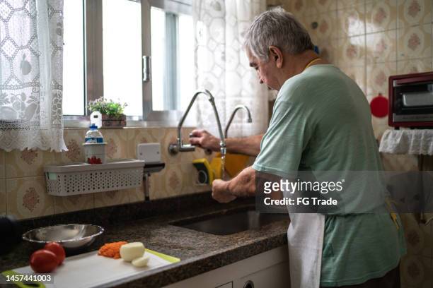 senior man washing hands in the kitchen sink at home - onion family stock pictures, royalty-free photos & images