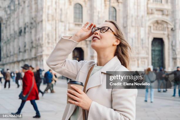 a woman tourist in italy looks at the architecture in milan's cathedral square and drinks take-out coffee - daily life at duomo square milan stockfoto's en -beelden