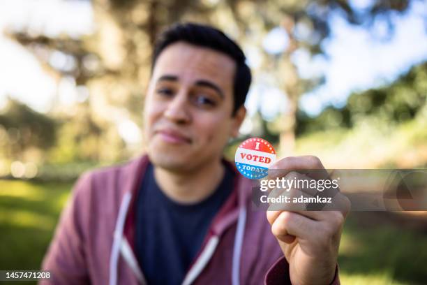 young mixed race hispanic man holding an i voted sticker - citizens head to the polls to vote in presidential election stockfoto's en -beelden