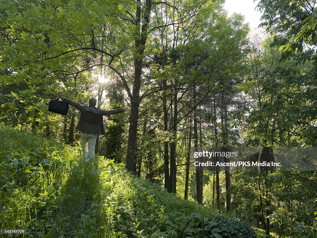 Businessman stands in forest, arms outstetched