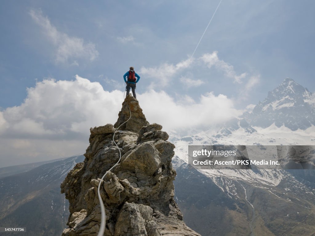 Climber stands on top of pinnacle, rope connects