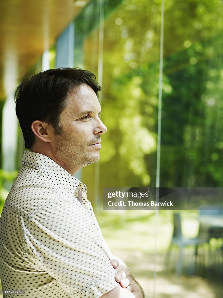 Man standing with arms crossed looking out window