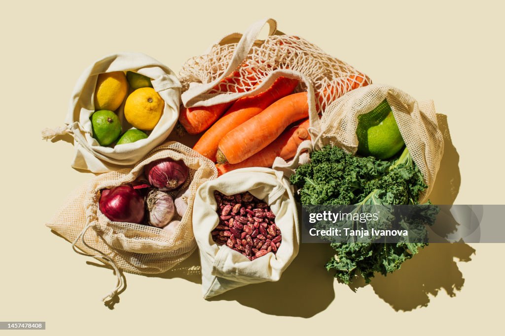 Variety Fresh of organic fruits and vegetables and healthy vegan meal ingredients in reusable eco cotton bags on beige background . Zero waste shopping concept. Healthy food, clean eating, eco friendly, no plastic. Flat lay, top view