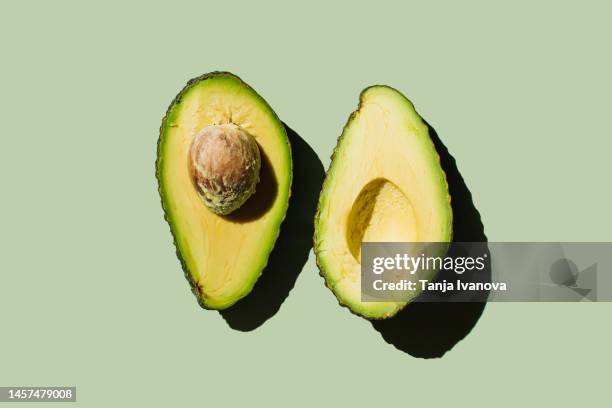 fresh ripe avocado fruit halves on green background. healthy food, diet and detox concept. flat lay, top view - avocado isolated stock-fotos und bilder