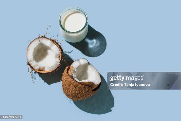 ripe coconuts and organic vegan coconut milk in glass on blue background. lactose-free milks in minimal flat lay style. top view, copy space - kokosmelk stockfoto's en -beelden