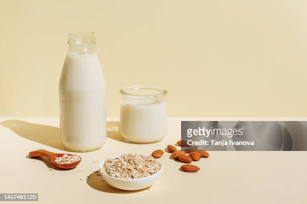 various organic vegan plant based milk in glasses and glass bottle and ingredients (nuts, oatmeal) on beige background. non dairy milk substitute drink, healthy eating. lactose-free milk in minimal style, copy space. - almond milk stock-fotos und bilder