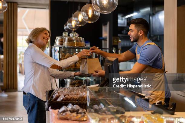 waiter giving a bag to a customer buying food at a cafe - pastry dough stock pictures, royalty-free photos & images