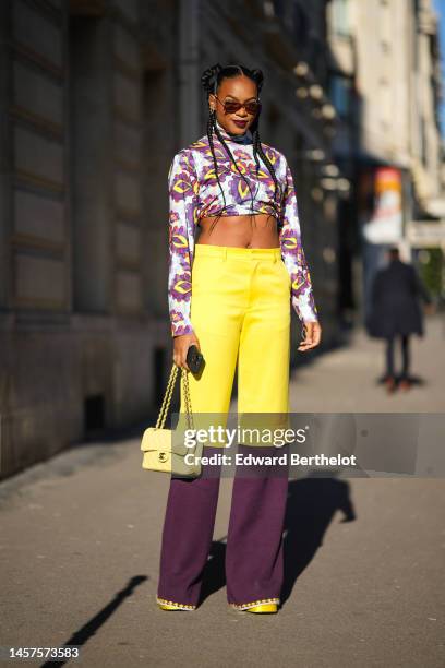 Didi Stone wears brown sunglasses, gold and diamonds earrings, a purple / yellow / orange / red print pattern turtleneck / long sleeves / cropped...