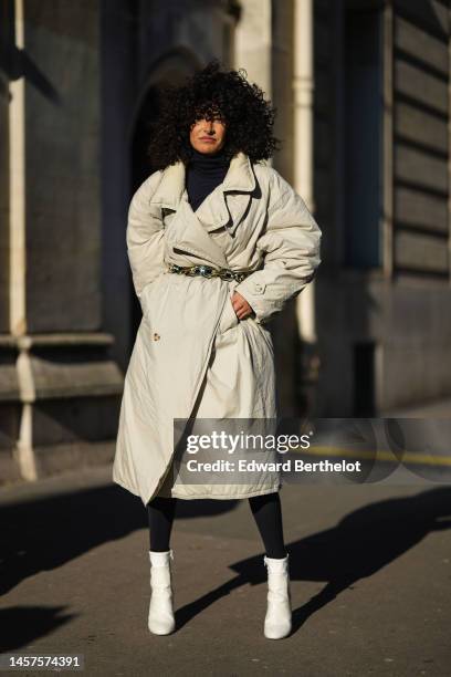 Brune Buonomano wears a navy blue wool turtleneck pullover, a beige long oversized belted puffer jacket, a black shiny leather shoulder bag, black...