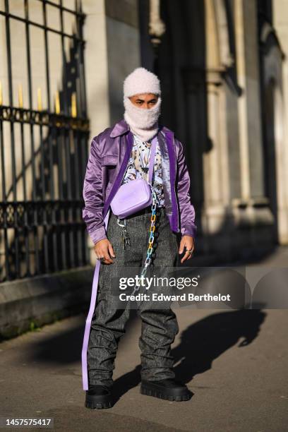 Theo Kimbaloula wears a pale purple fluffy balaclava, a pale yellow with navy blue / brown print pattern pullover, a purple shiny nylon bomber coat,...