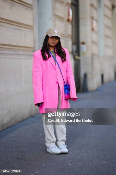 Guest wears a beige with embroidered LA embroidered pattern cap, a brown t-shirt, a gold chain pendant necklace, pale pink and white pearls...