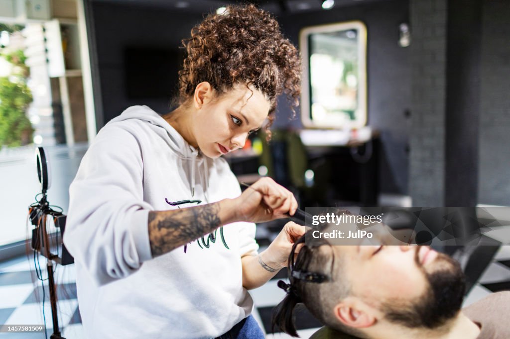 Young female hairdresser braiding hair to client at barber shop
