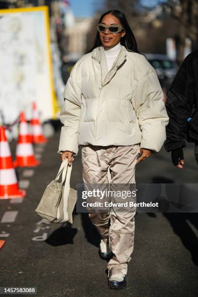 Guest wears khaki matte plastic square sunglasses, a white turtleneck pullover, a white latte matte oversized puffer jacket, brown gold shiny nylon...