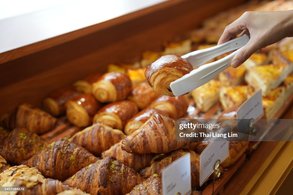 Close-up woman choosing pastry from a bakery store selecting holding a tray and service tong