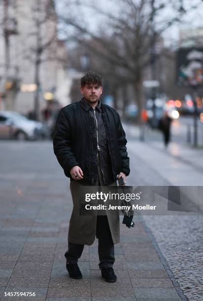 Noah Kächelin seen wearing Adidas gazelle sneaker, black leather jacket, black bomber jacket, green long coat, black trousers and a small black bag...