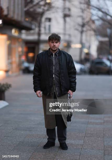 Noah Kächelin seen wearing Adidas gazelle sneaker, black leather jacket, black bomber jacket, green long coat, black trousers and a small black bag...