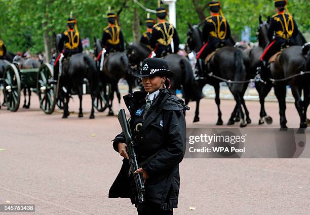 An armed police officer stands guard as soldiers wearing ceremonial uniforms move along The Mall to take their positions during the Diamond Jubilee...