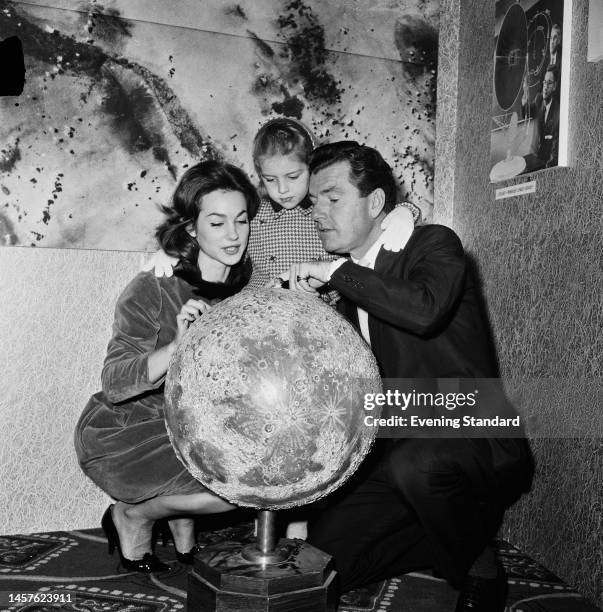 British actors Shirley Anne Field and Kenneth More , stars of the film 'Man in the Moon', look at a model of the moon with More's daughter Sarah, on...