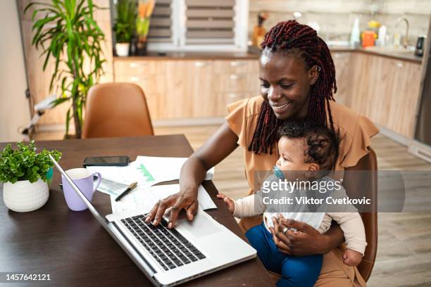 working from home. mother at home reviews finances on the laptop with baby in her lap - save our future babies stock pictures, royalty-free photos & images