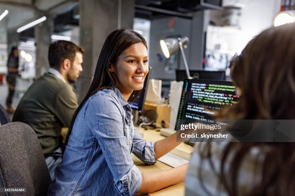 Happy female programmer talking to her colleague in the office.