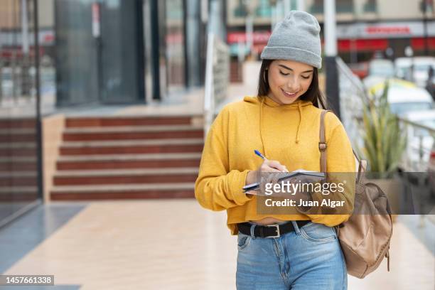 positive female student writing down thoughts in diary on street - yellow note pad stock pictures, royalty-free photos & images