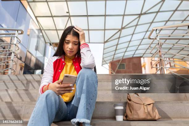 teen girl reading unpleasant messages on mobile phone - whatsapp stockfoto's en -beelden